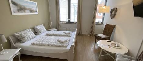 Habitación de hotel con cama doble, una mesita, una silla y una ventana con cortinas.