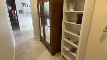A hallway with a wooden wardrobe and a white shelving unit against a plain wall.