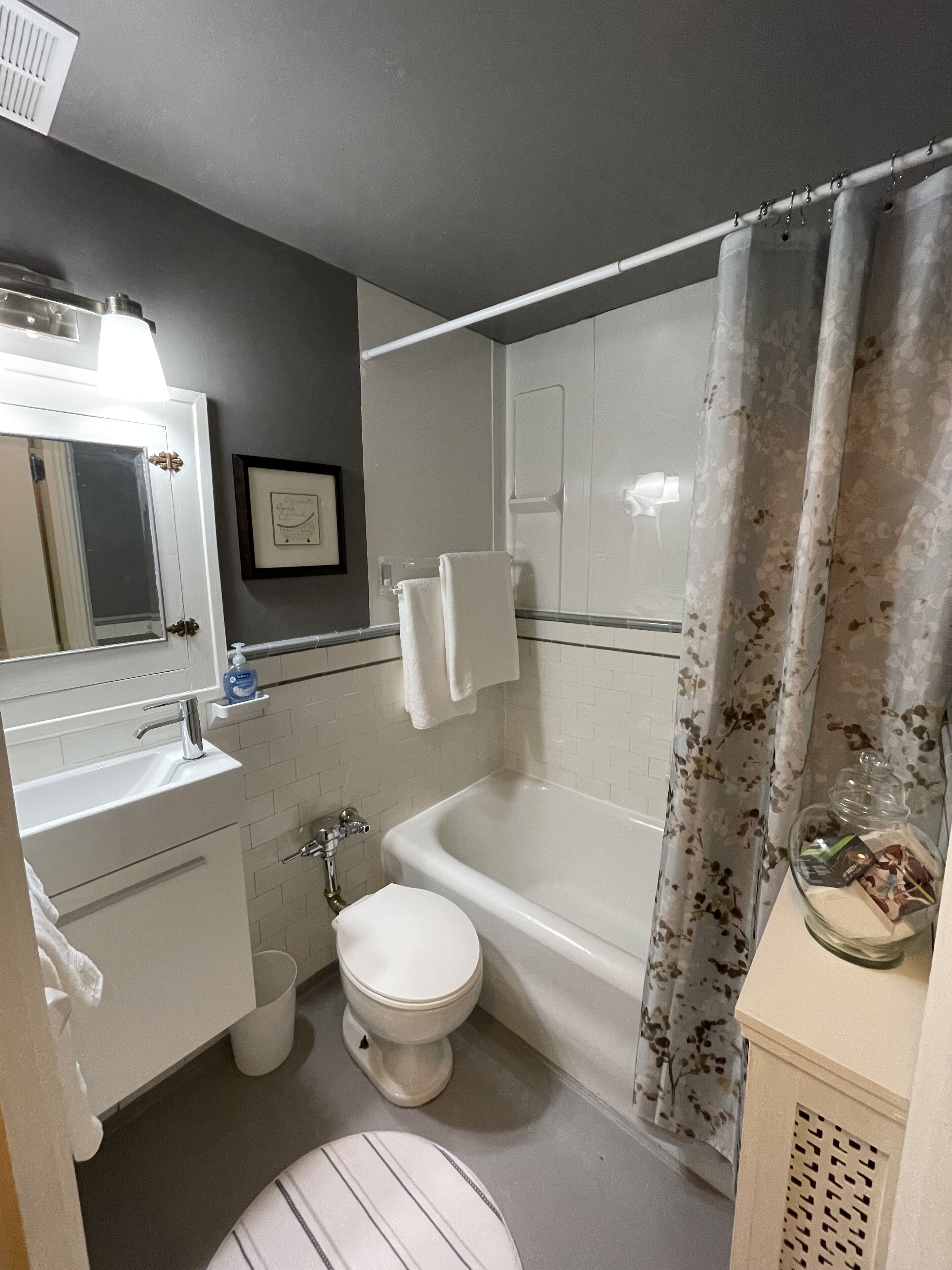 Un baño con lavamanos, inodoro y bañera blancos. Hay una cortina de ducha con estampado floral.