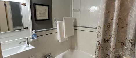 Un baño con lavamanos, inodoro y bañera blancos. Hay una cortina de ducha con estampado floral.