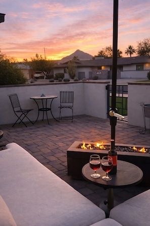 A rooftop patio with a fire pit, two chairs, a table, and a bottle of wine.