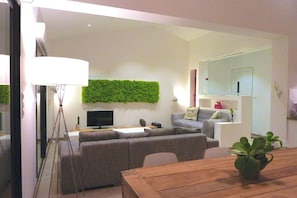 Un salon moderne avec un mur vert, un ensemble de canapés, une table en bois et un téléviseur.