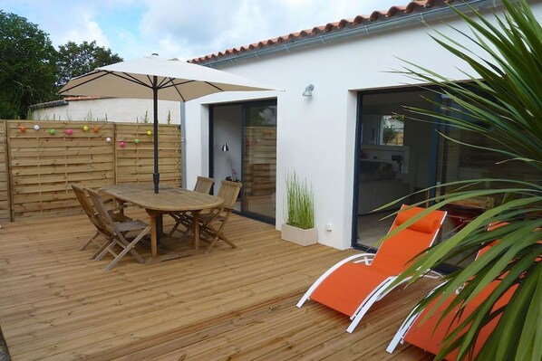 Eine Holzterrasse mit Tisch und Stühlen, eine Glastür zu einem Zimmer und ein orangefarbener Sessel.