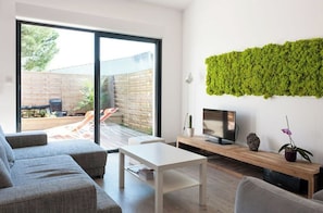 Un salon moderne avec un canapé, une table basse, un téléviseur posé sur un meuble en bois et une œuvre d’art murale de couleur verte.