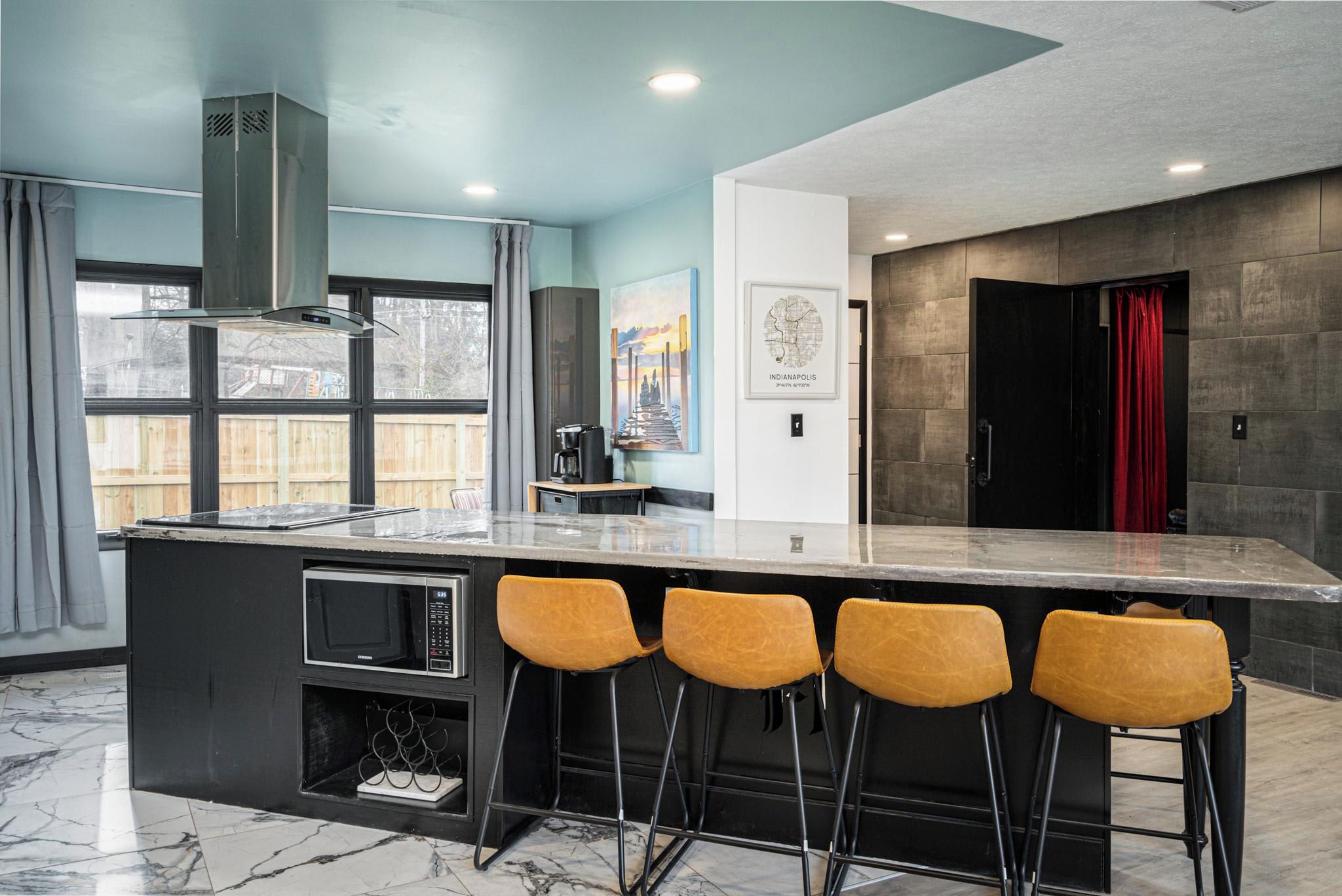 A modern kitchen with a central island, bar stools, a microwave, and a red curtain.