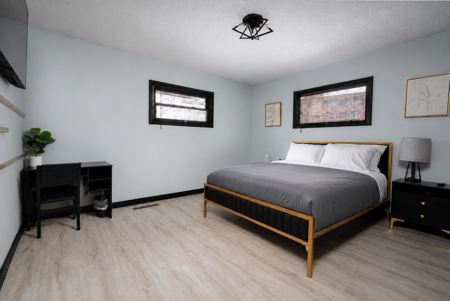 A bedroom with a bed, a desk, a chair, a lamp, and two windows.