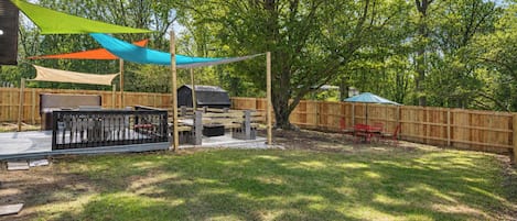 A backyard with a barbecue area, a wooden fence, and a tree providing shade.