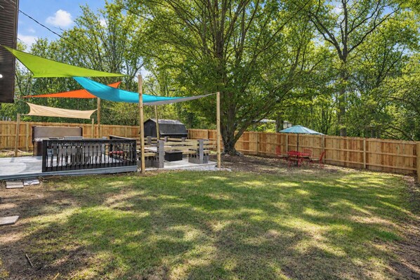 A backyard with a barbecue area, a wooden fence, and a tree providing shade.