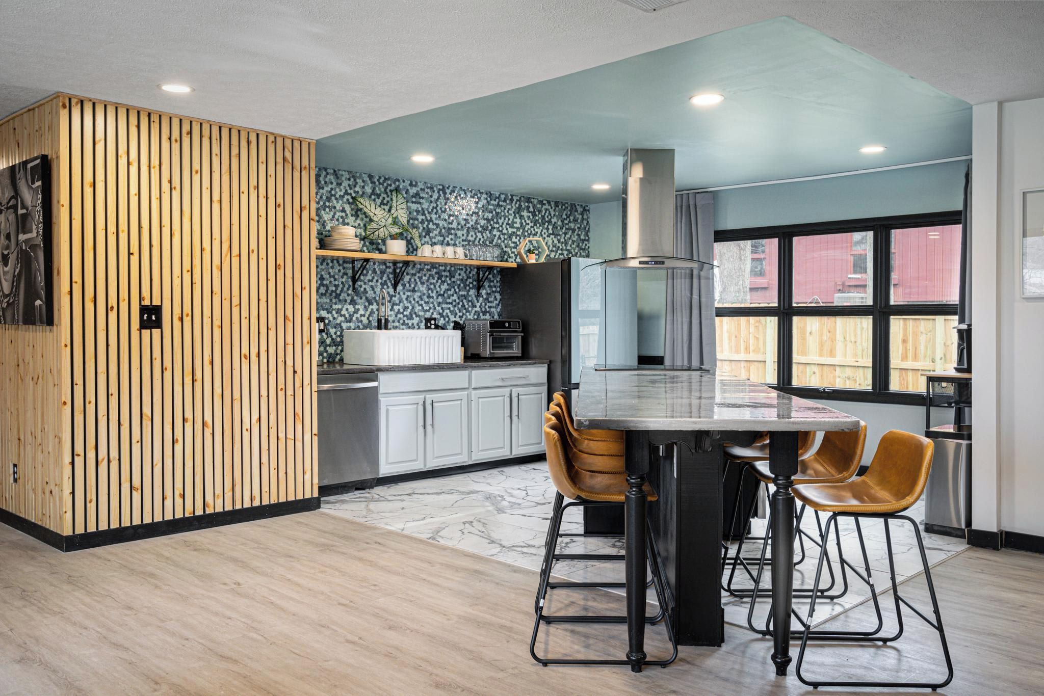 A modern kitchen with a wooden accent wall, a marble backsplash, and a large window.
