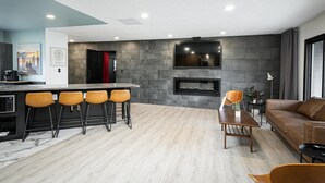 Una sala de estar moderna con chimenea, un área de bar con taburetes y un sofá de cuero.