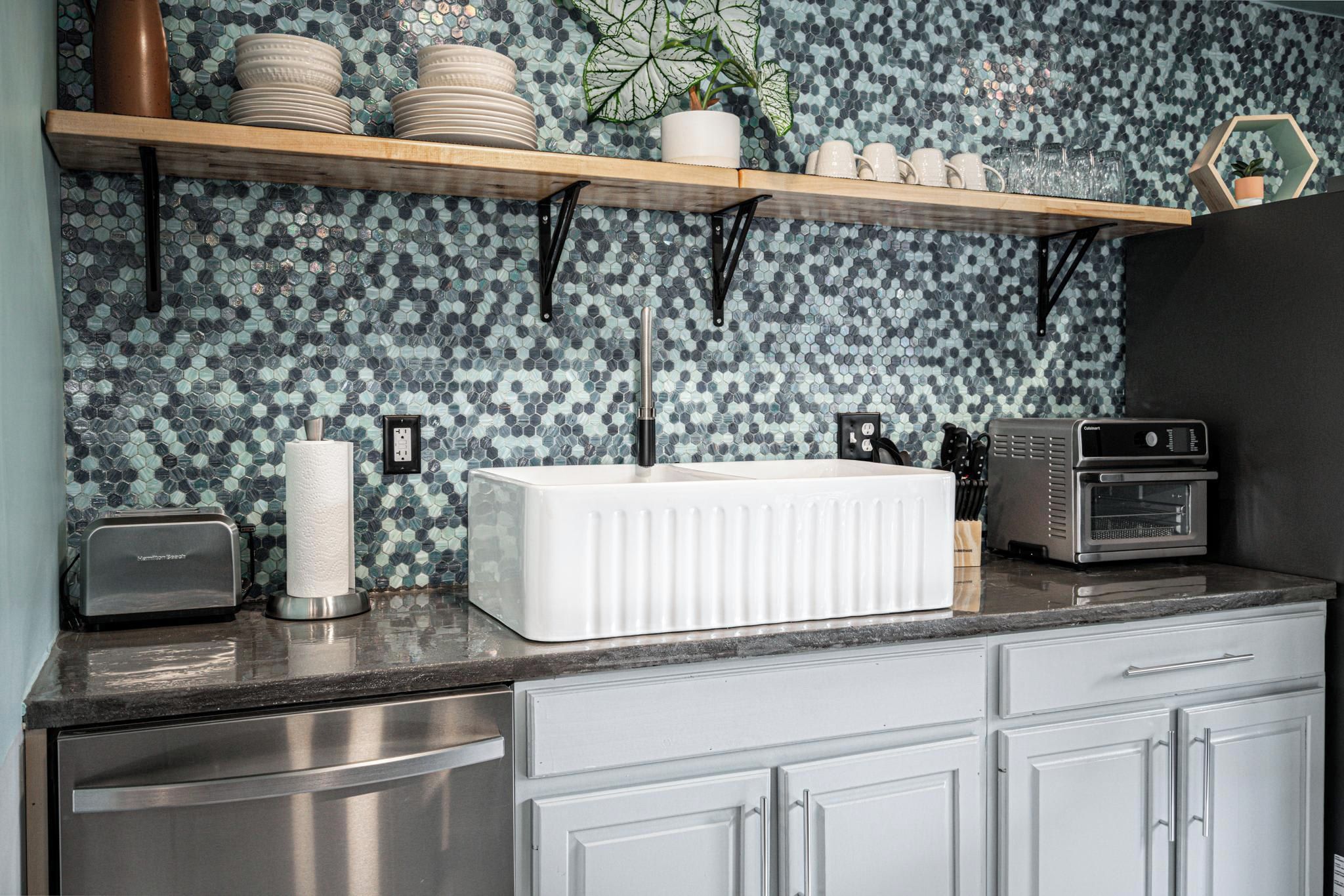 A kitchen with a tiled backsplash, a white countertop, a toaster, a kettle, and a coffee maker.