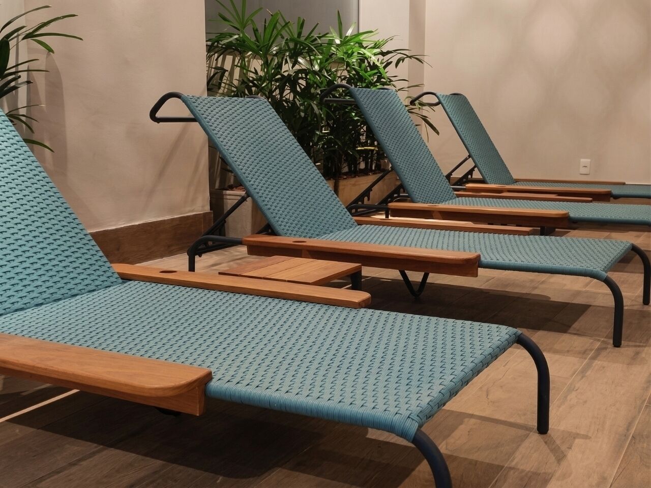 Een rij comfortabele stoelen met houten leuningen en blauwe stoffen rugleuningen, op een houten vloer, met potplanten op de achtergrond.