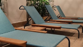Een rij comfortabele stoelen met houten leuningen en blauwe stoffen rugleuningen, op een houten vloer, met potplanten op de achtergrond.