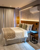 Una habitación de hotel moderna con una cama grande, una mesita de noche, aire acondicionado montado en la pared y una lámpara colgante.