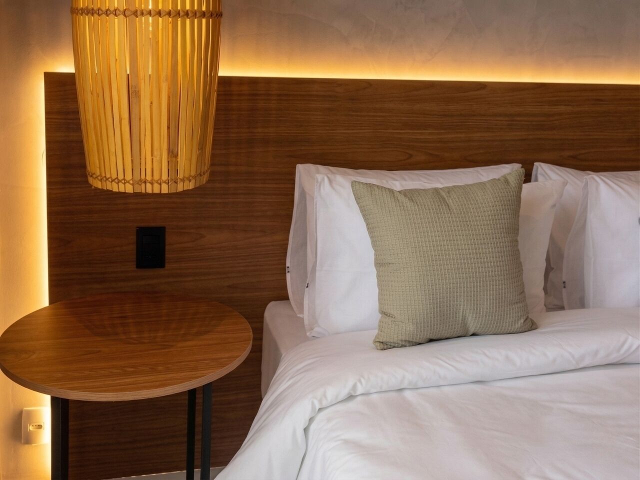 A hotel room with a wooden headboard, a round wooden table, and a bed with white bedding and a green pillow.