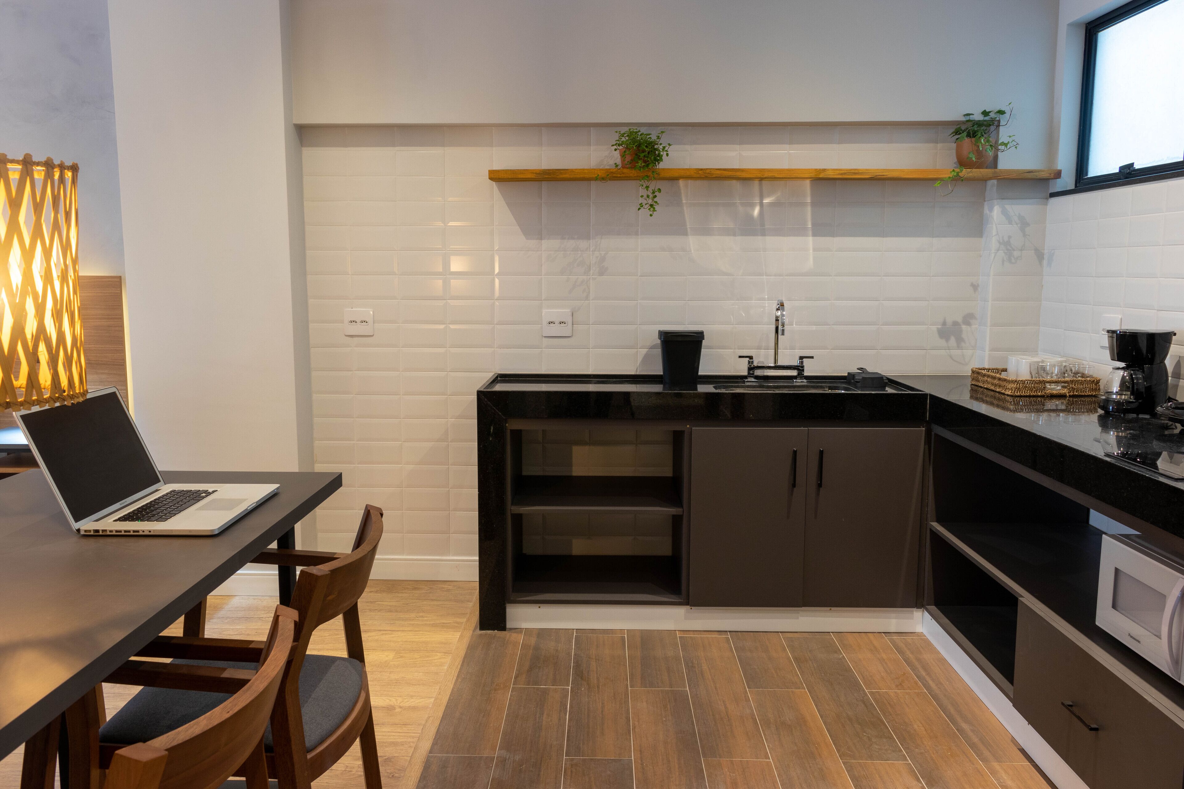 A modern kitchen with a black countertop, wooden cabinets, and a built-in oven. There is a laptop on a table and a plant on the shelf.