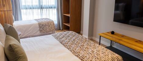 A hotel room with two beds, a wooden wardrobe, a TV, and a bench.