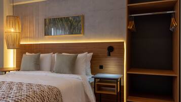 Une chambre d’hôtel moderne avec un grand lit, une tête de lit en bois, une table de chevet, une lampe fixée au mur et un porte-manteau.