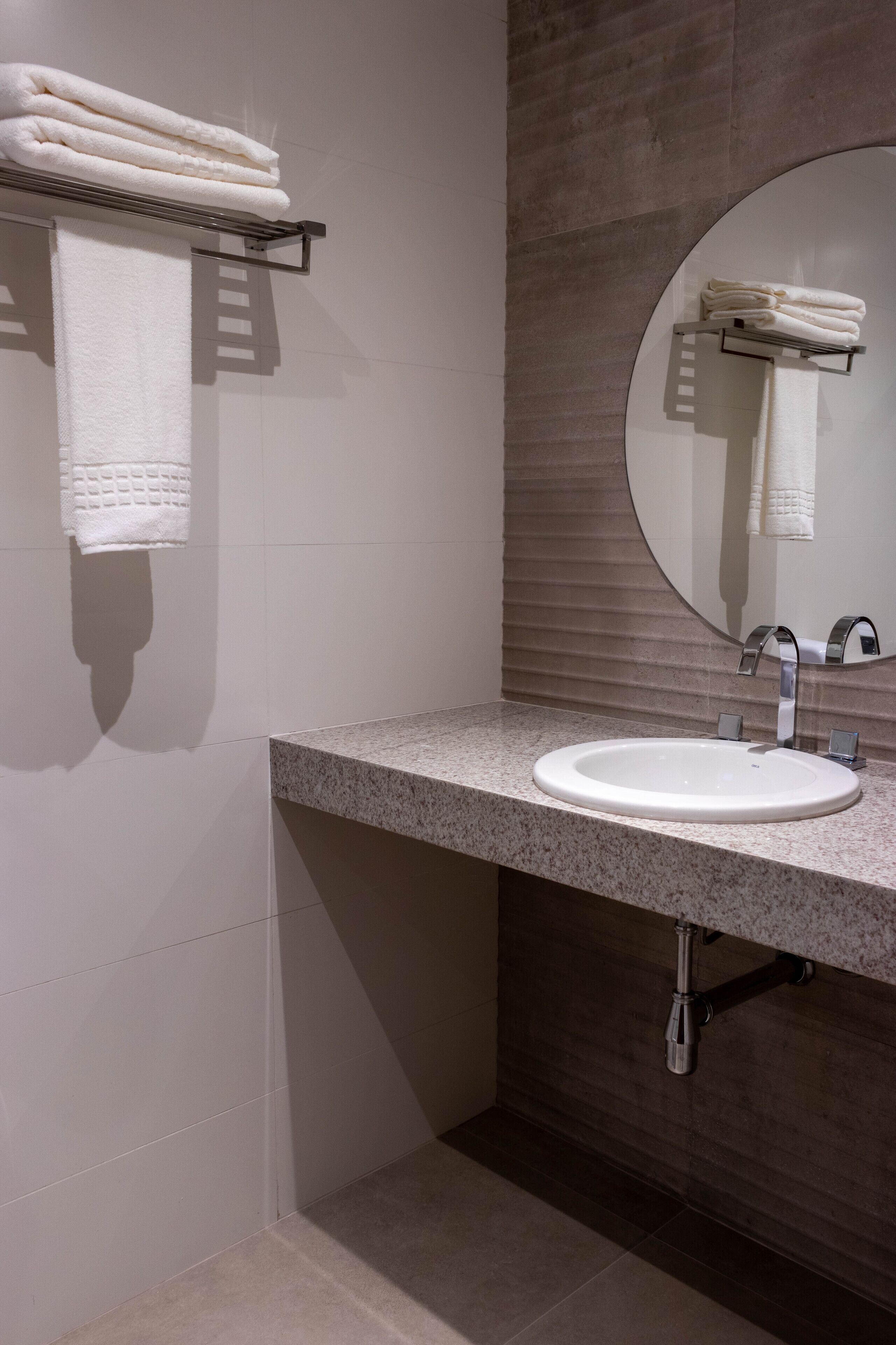 Un baño con un espejo redondo, un lavabo y barras para toallas.