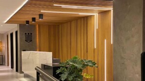 A modern reception area with a marble reception desk, a potted plant, and a wooden slatted wall. - Kastel Petrópolis (Petrópolis)