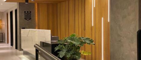 A modern reception area with a marble reception desk, a potted plant, and a wooden slatted wall.