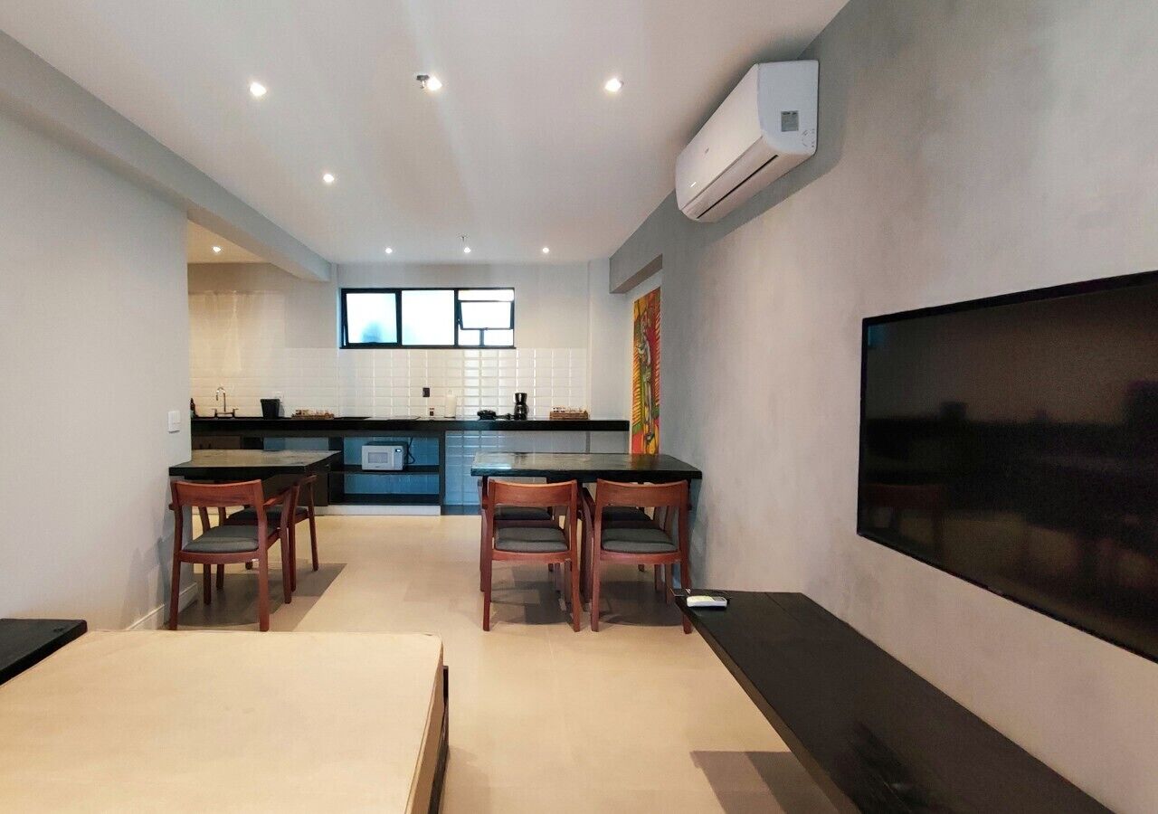 A modern kitchen with blue cabinets, a dining area with wooden chairs, and a large flat-screen TV mounted on the wall.