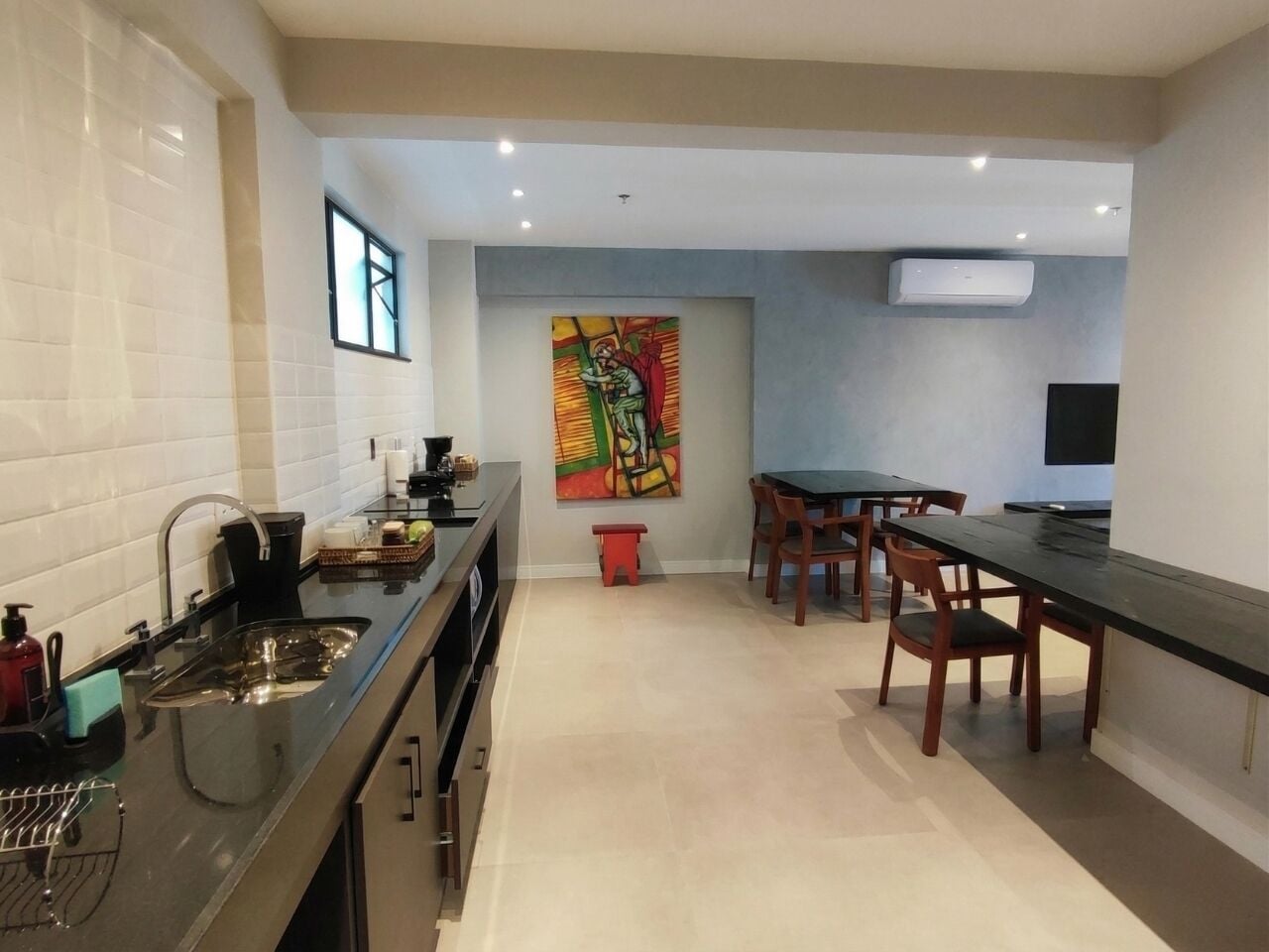A modern kitchen with a dining area, a window, and a colorful artwork on the wall.