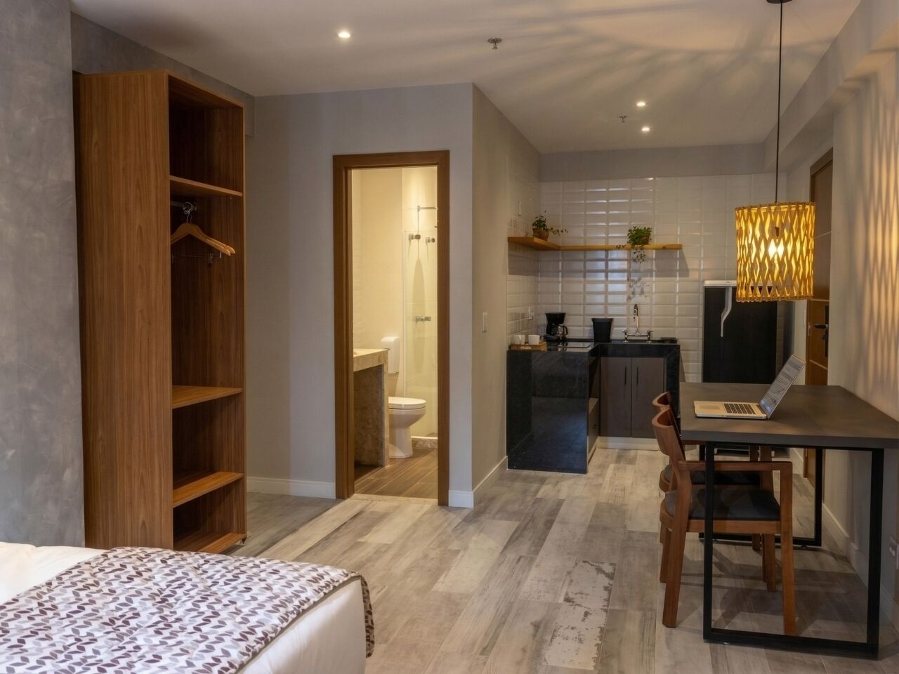 A modern bedroom with a bed, a wooden wardrobe, and a desk with a laptop.