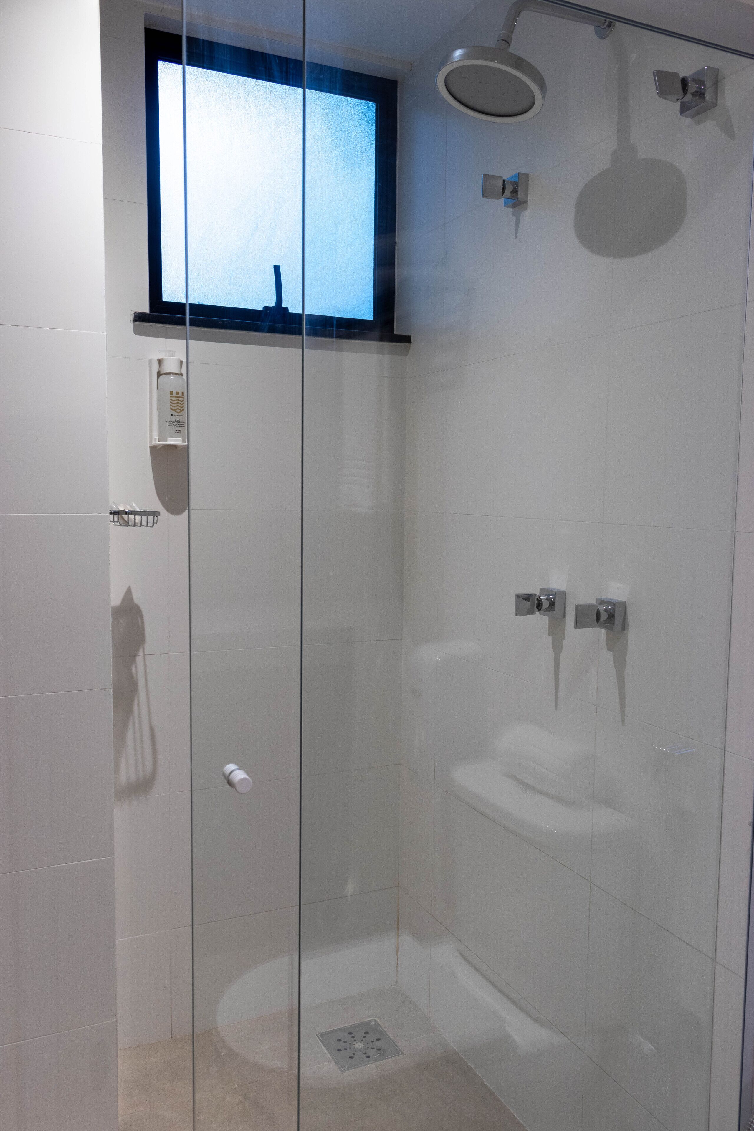 A modern shower area with a glass door, a window above, and a handheld showerhead.
