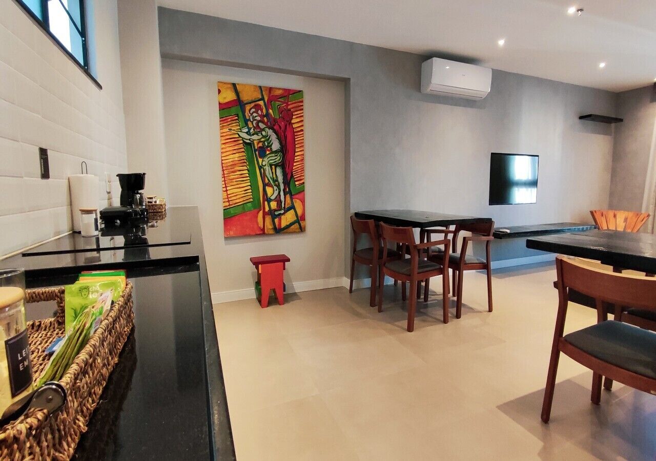 Een moderne keuken met een eetgedeelte, een kleurrijk abstract schilderij en een flatscreen televisie.