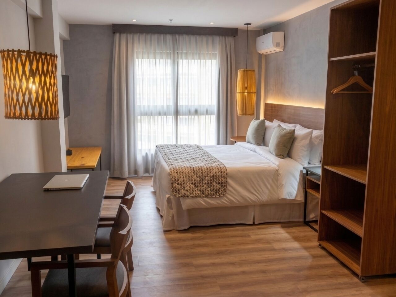 Een moderne hotelkamer met een bed, nachtkastje, lamp, kast en bureau met een laptop.