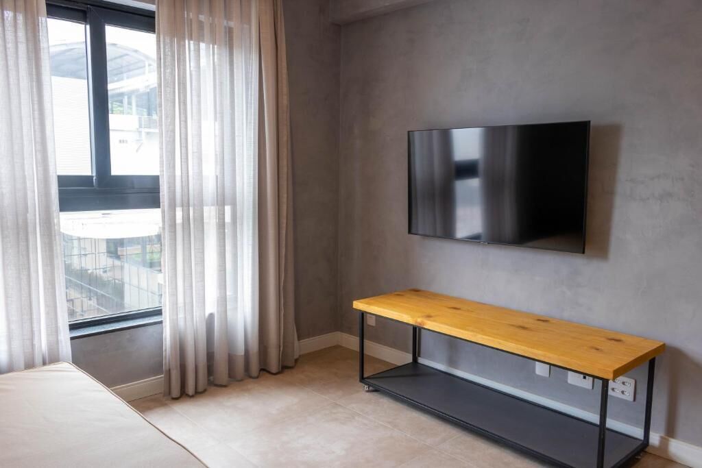 A modern room with a large window, a flat-screen TV mounted on the wall, and a wooden bench.