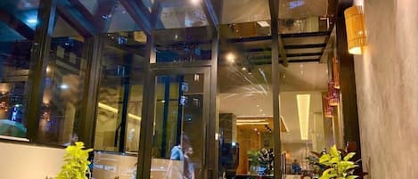 A hotel entrance with glass doors, potted plants, and a modern interior visible through the glass.