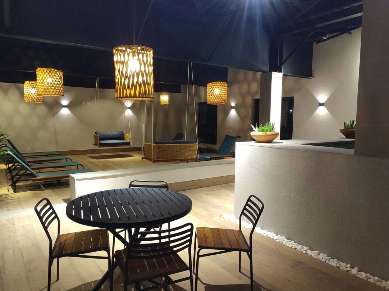 Un espacio al aire libre con mesa redonda y sillas, rodeado de sillones de descanso y una piscina pequeña.
