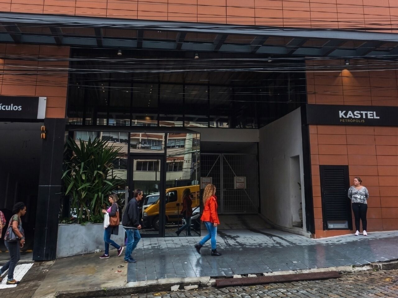 La entrada de un edificio con un toldo negro, una furgoneta amarilla estacionada en el interior y un letrero que dice 'KASTEL PETROPOLIS'.