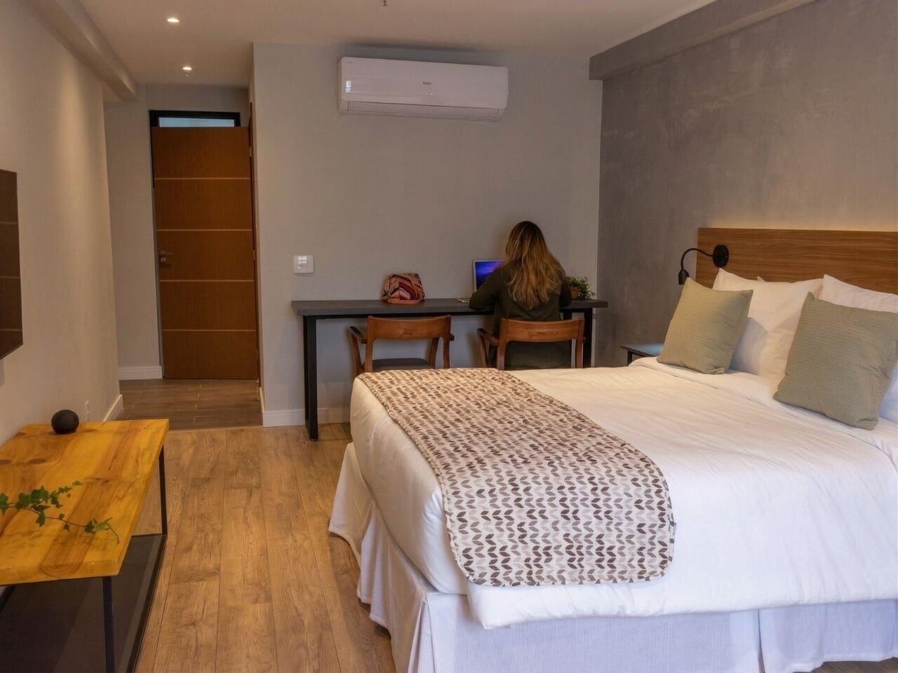 Quarto de hotel com uma cama, uma escrivaninha, uma cadeira e um aparelho de ar condicionado.