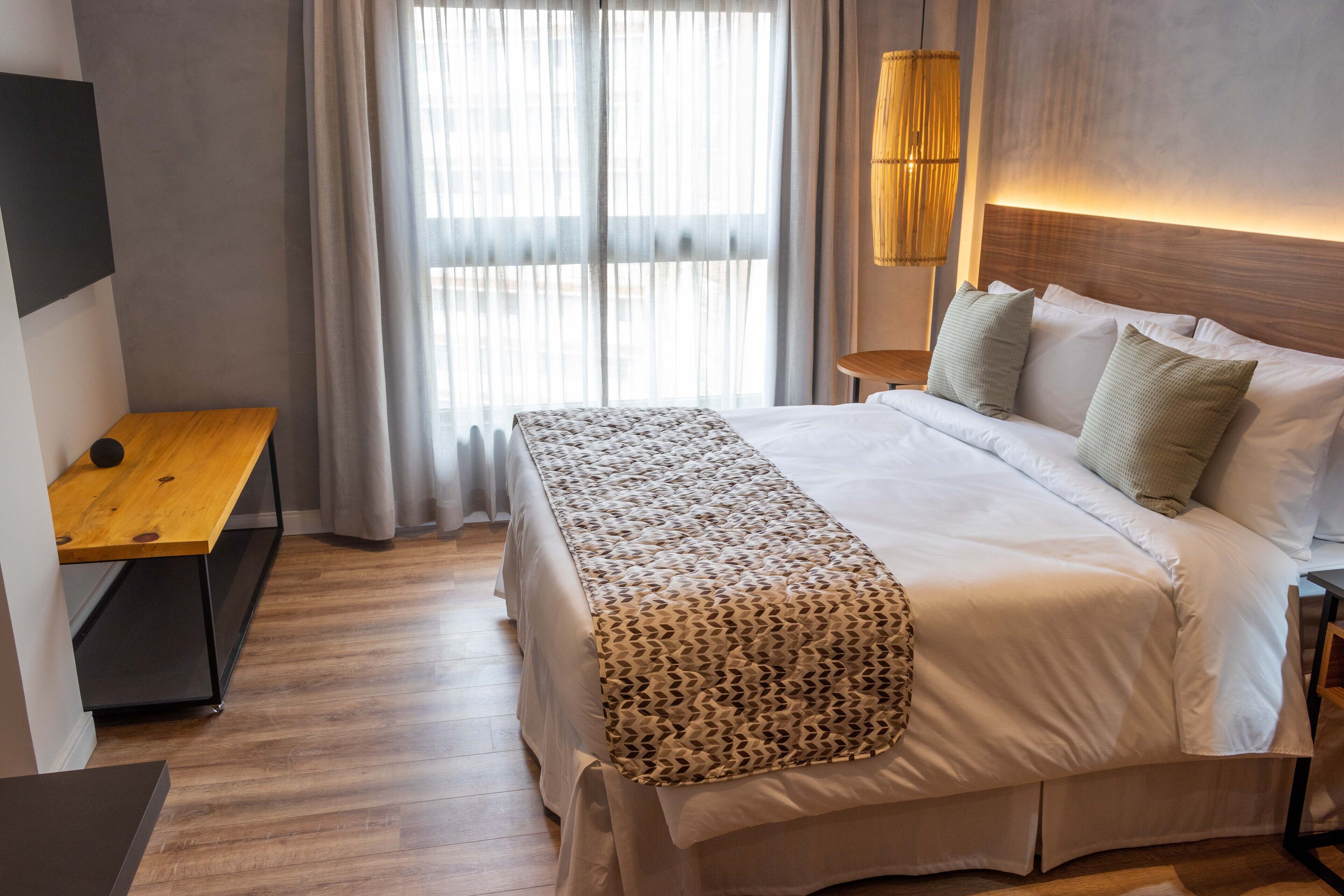 Ein modernes Hotelzimmer mit einem großen Bett, einer hölzernen Sitzbank, einem Nachttisch und einer Lampe.