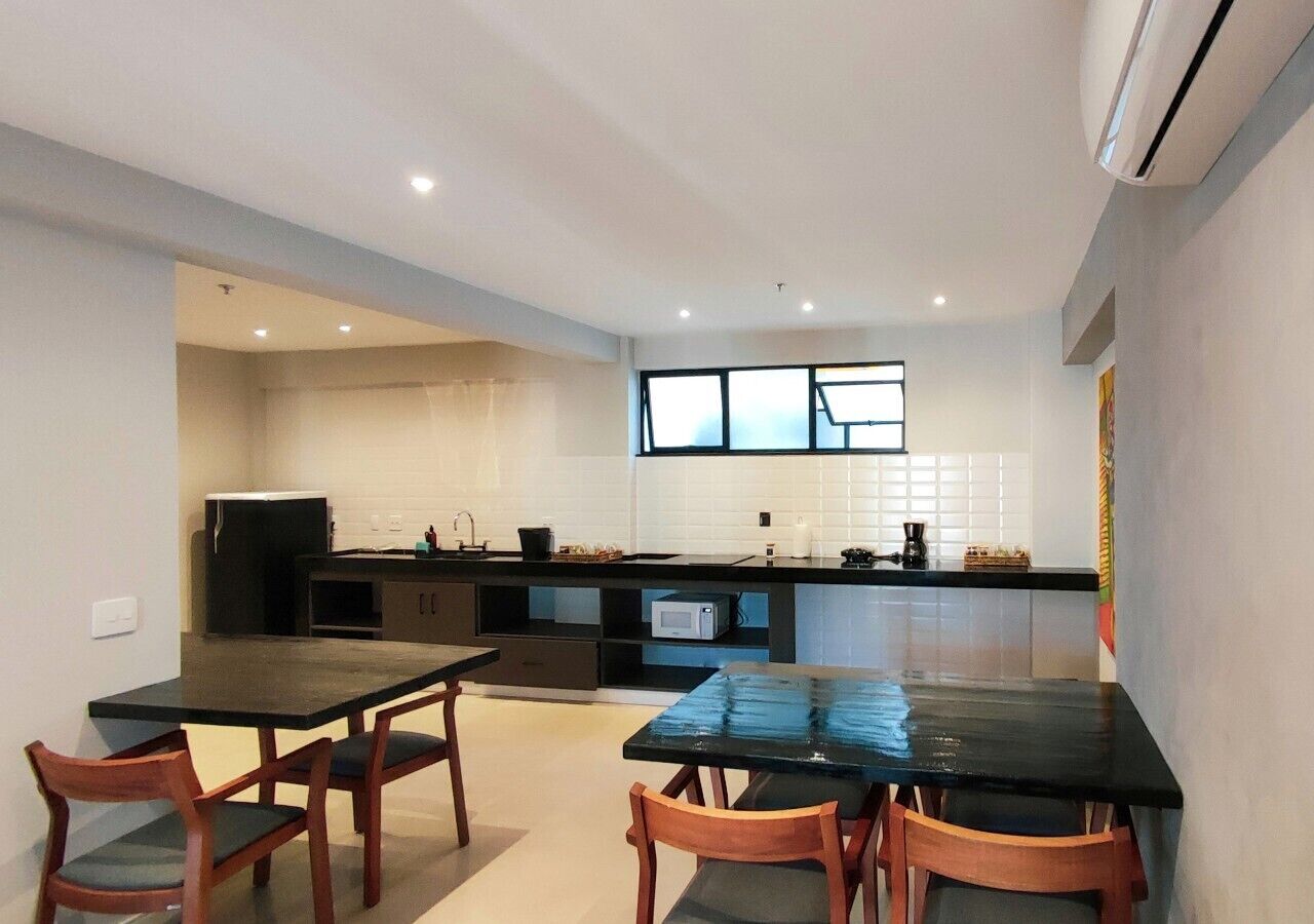 Una cocina moderna con comedor, que incluye una mesa y sillas negras, un microondas y un ventanal grande.