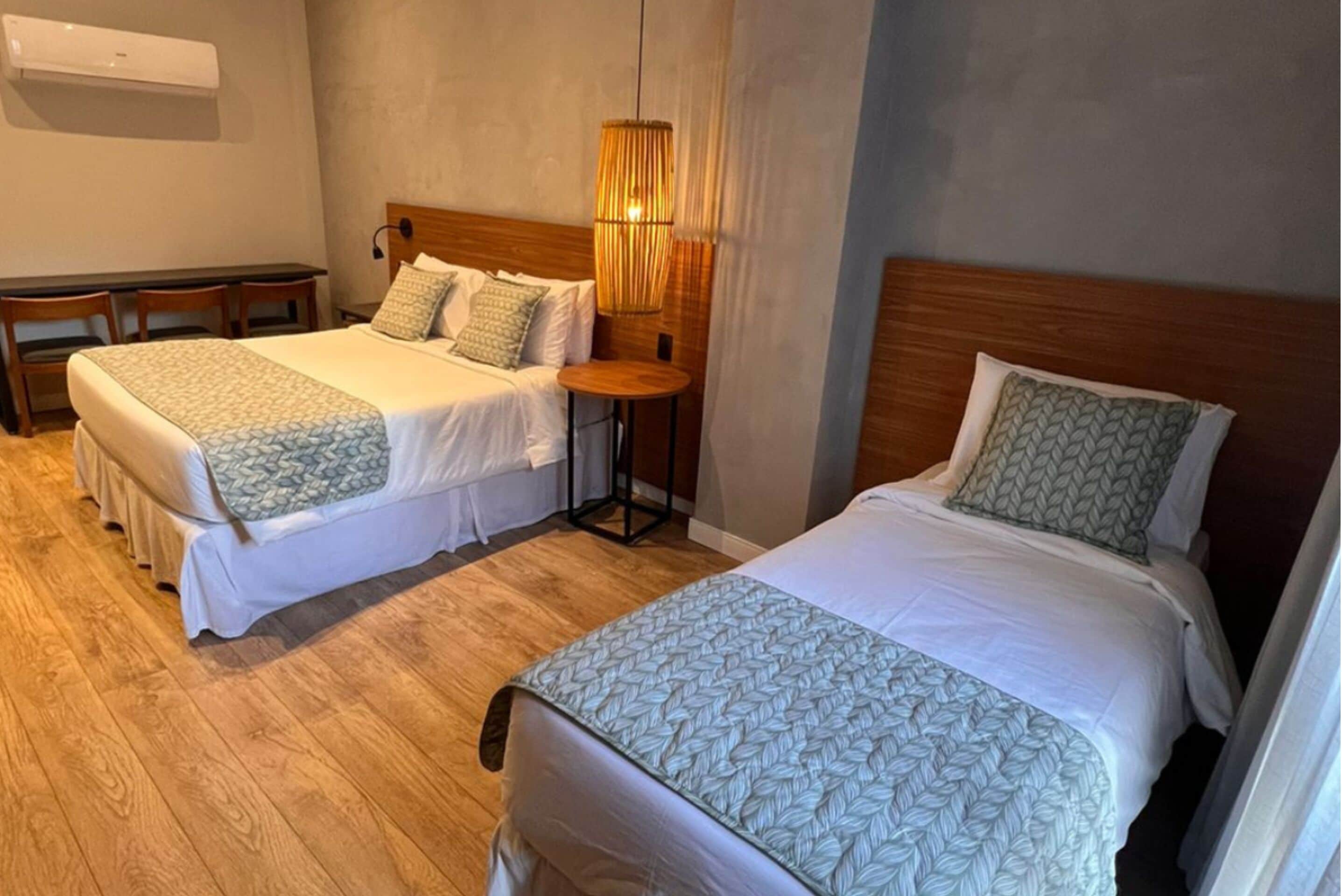 Two single beds with wooden headboards, a small round table, and a wall-mounted air conditioner.