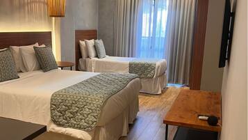 A hotel room with two beds, a wooden table, a TV, and a window with curtains.