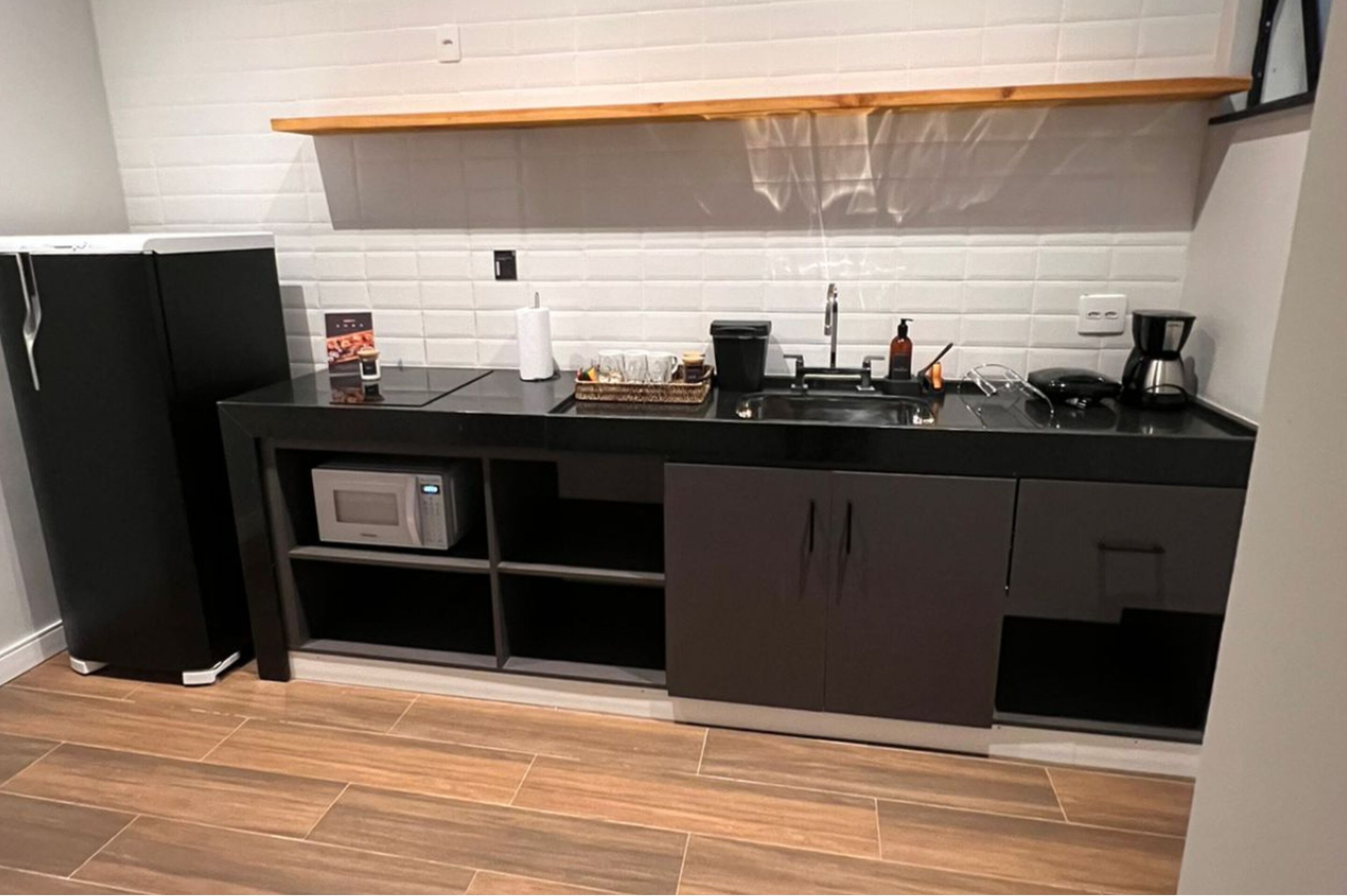 A compact kitchen with a black countertop, a microwave, a coffee maker, and a small refrigerator.