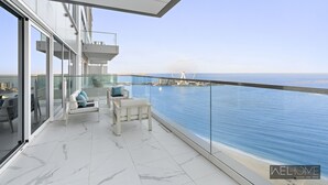 Een modern balkon met glazen hekwerk met uitzicht op een wateroppervlak en een verre brug.