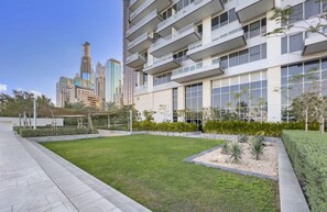 A modern building with multiple balconies, a well-maintained lawn, and a clear view of the city skyline in the background. - WelHome - Deluxe Apartment With Direct Access to the Beach (Dubai)