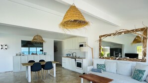 Un amplio espacio habitable con una mesa de comedor, sillas, un sofá con cojines, una mesa baja y una cocina al fondo.