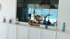Una habitación con un ventanal grande que da al mar, un armario blanco con objetos decorativos y una lámpara colgante de mimbre.