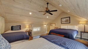 A bedroom with two beds, a ceiling fan, a painting, and a lamp.