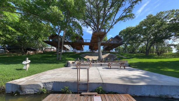 A park with a wooden deck, picnic tables, and a concrete platform with a treehouse structure.