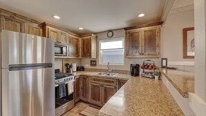 A kitchen with wooden cabinets, stainless steel appliances, a granite countertop, and a window with a view.