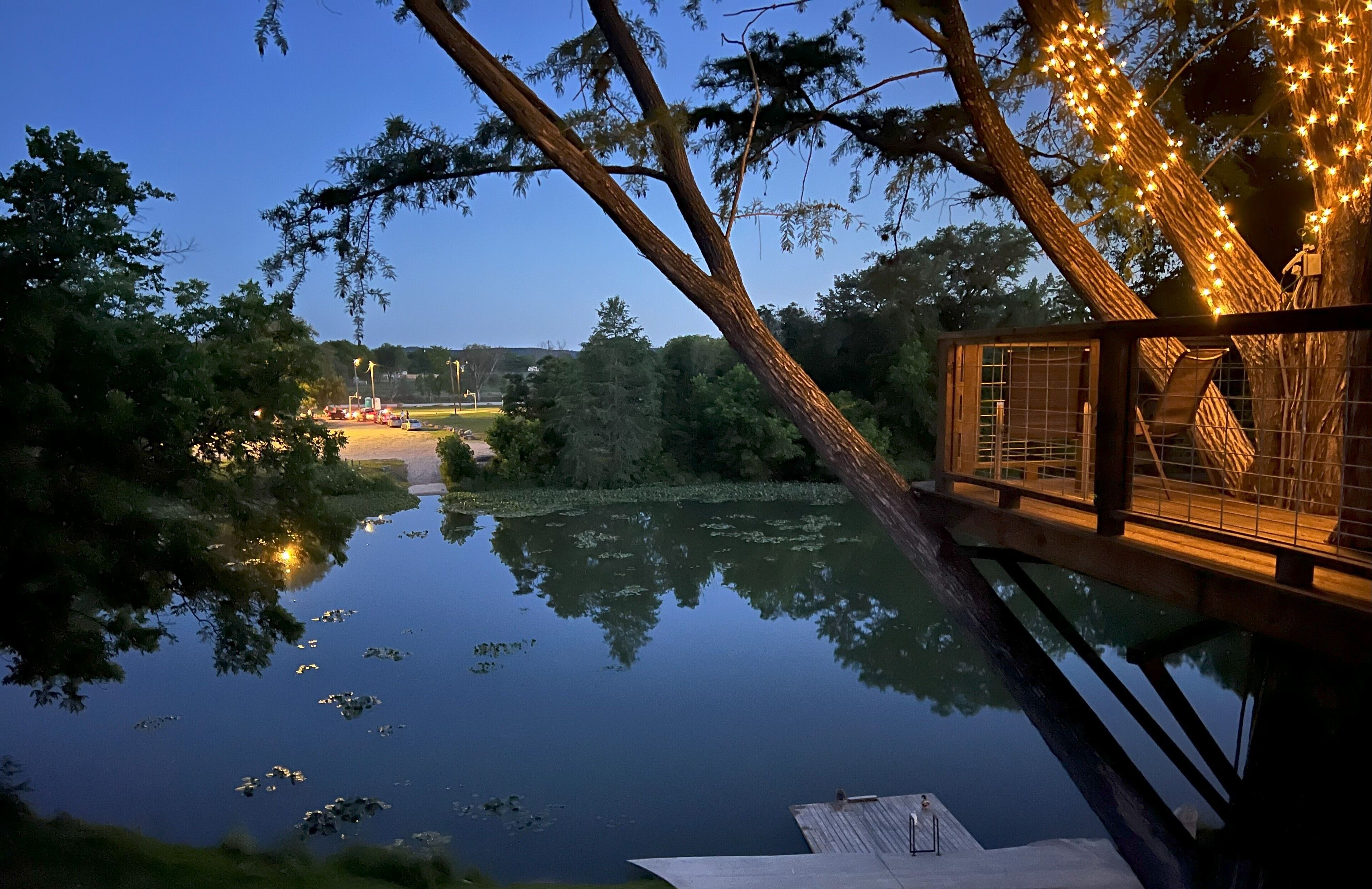 A wooden deck overlooking a calm lake with reflections of trees and lights.