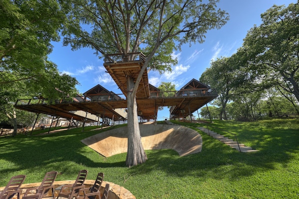 A treehouse structure with multiple levels, connected by wooden walkways, set in a grassy area with a clear sky.